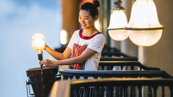 A person standing on a balcony with a railing, holding a light bulb. There are two hanging lamps on the wall behind them.