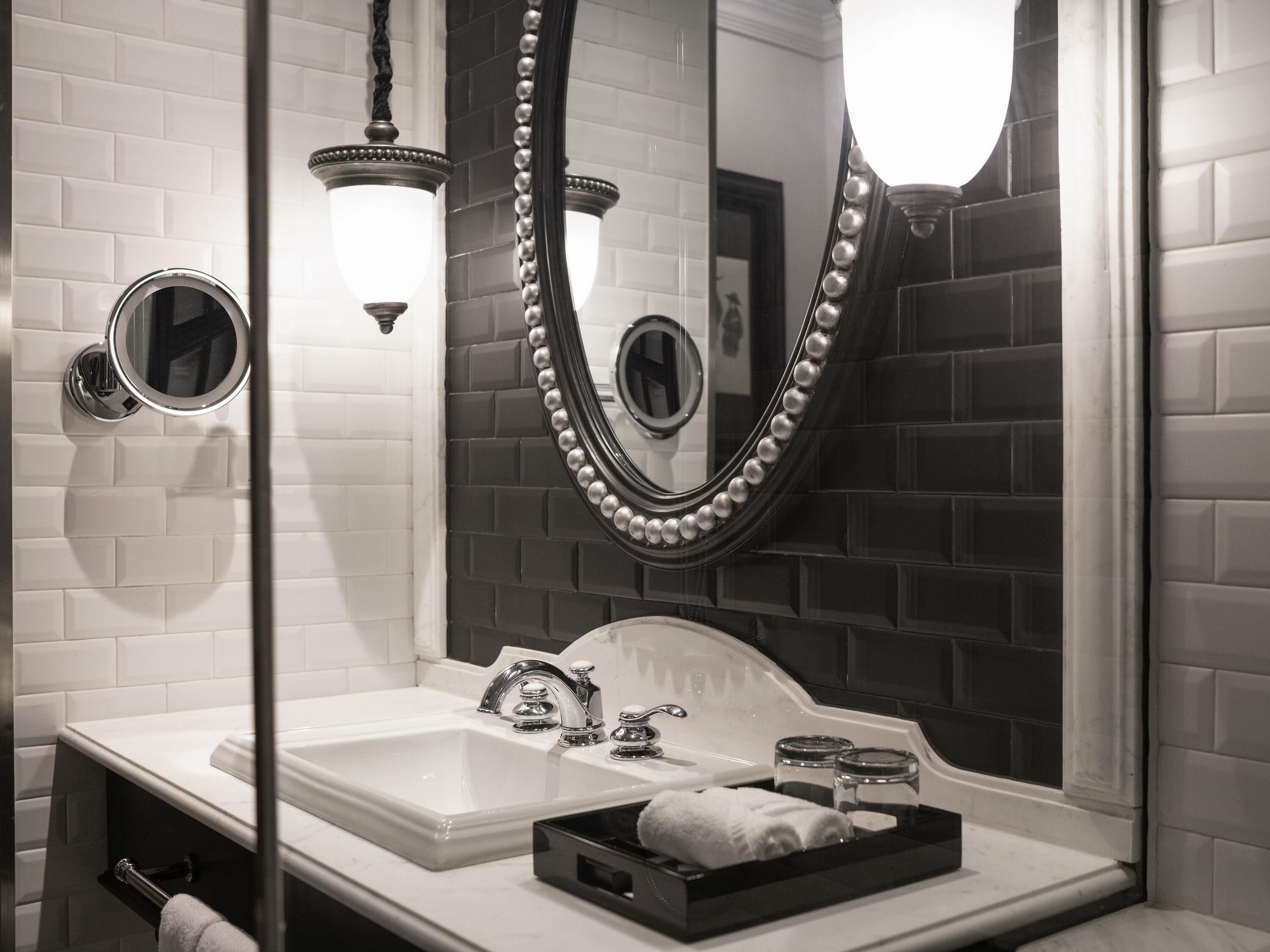 A modern bathroom with a white sink, two faucets, a large mirror with pearl bead trim, and a towel rack.