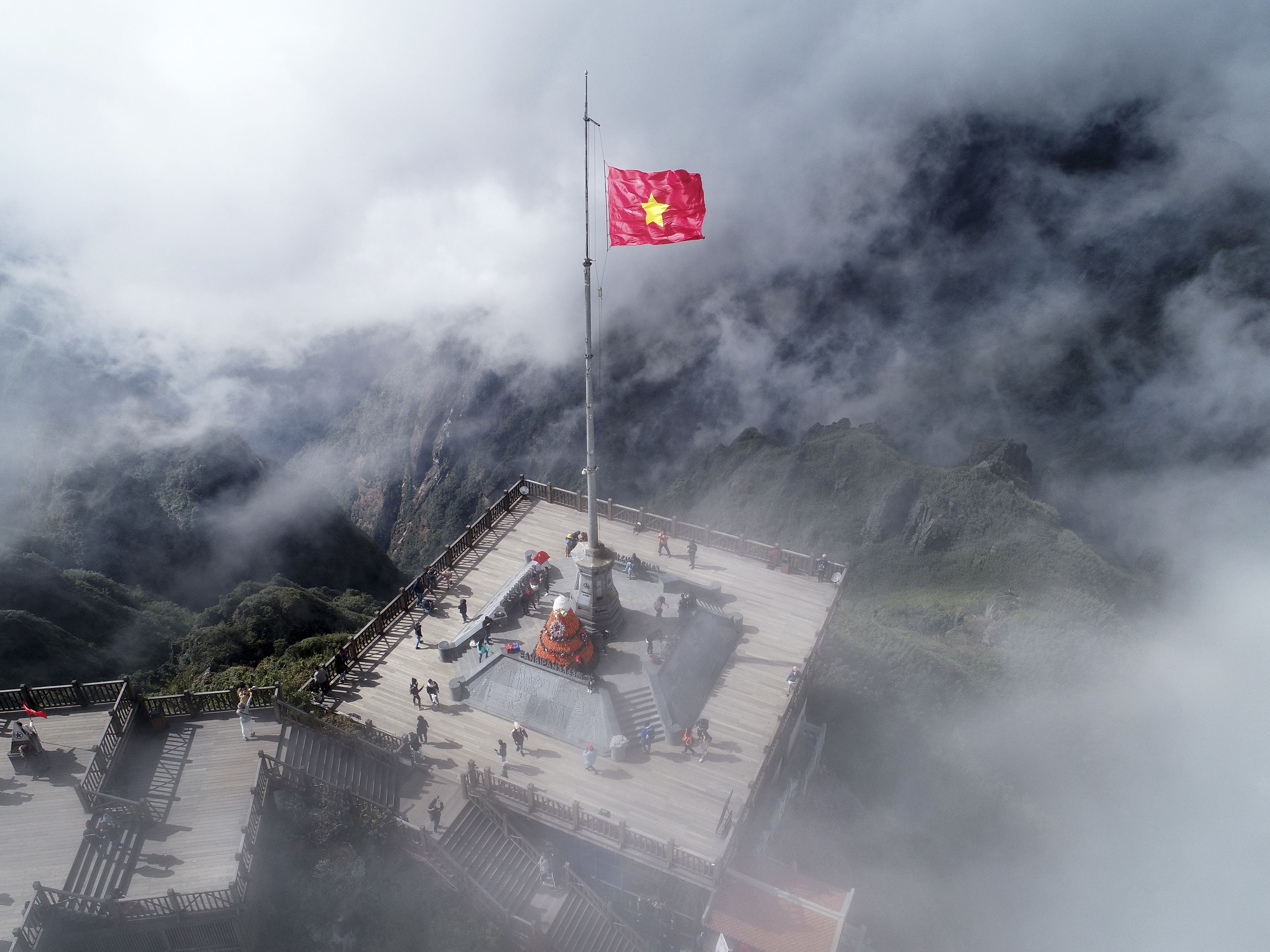 A high-altitude viewpoint with a flagpole, wooden platform, and surrounding mountainous terrain.