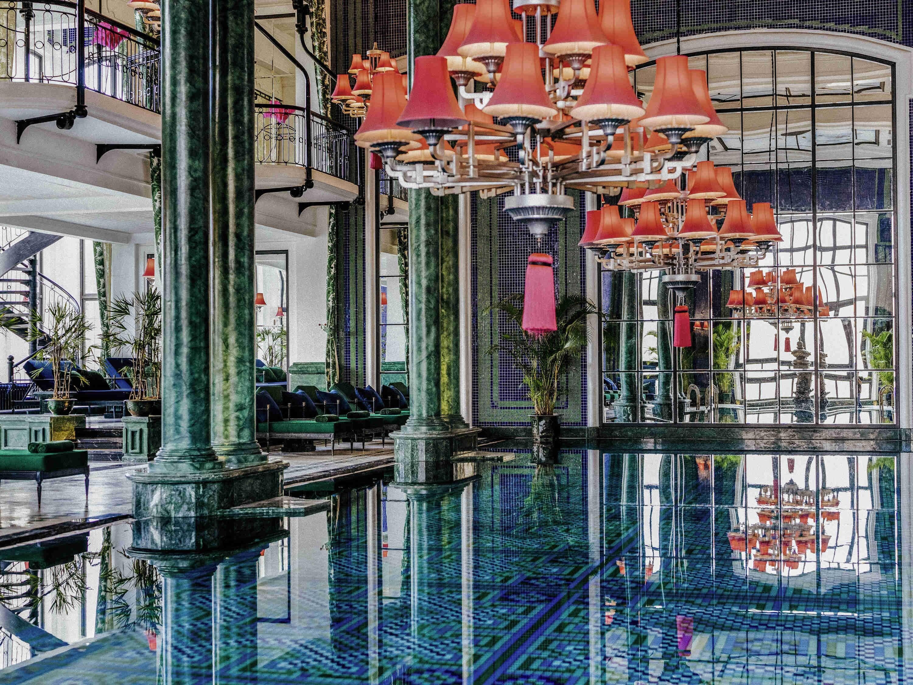 Eine großzügige Lobby mit einem zentralen Spiegelbecken, verschiedenen Sitzbereichen und einer imposanten Treppe.