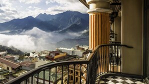 Un balcón con vistas a montañas y nubes, una escalera y un edificio con suelo a cuadros.