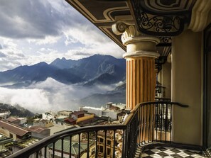 Un balcón con vistas a montañas y nubes, una escalera y un edificio con suelo a cuadros.
