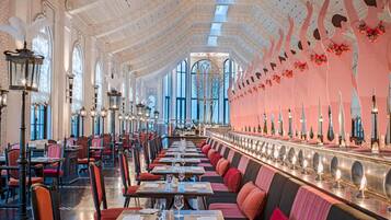 Ein geräumiges, elegant eingerichtetes Restaurant mit hohen Decken, aufwendigen Kronleuchtern und einem langen Speisebereich mit komfortablen Sitzmöglichkeiten.