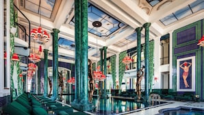 Un lobby lujoso con asientos verdes, una piscina central y columnas ornamentadas.