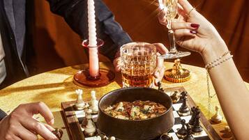 Ein Schachbrett mit Figuren, eine Schale mit Essen und ein Glas Trank auf einem Tisch.