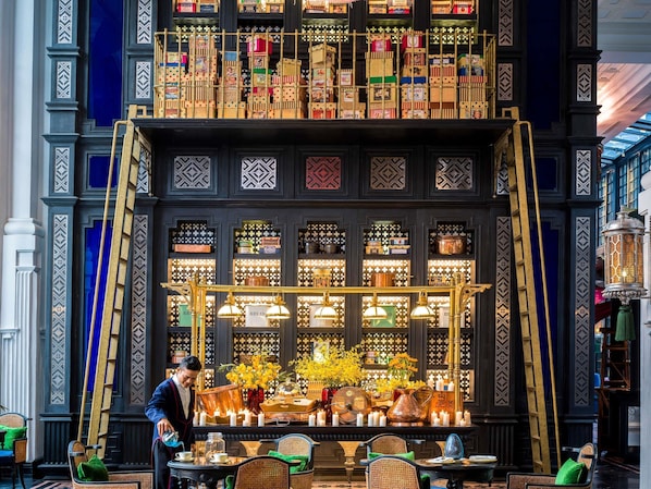 A hotel lobby with a central display of food items, a chandelier, and a person attending to the display.