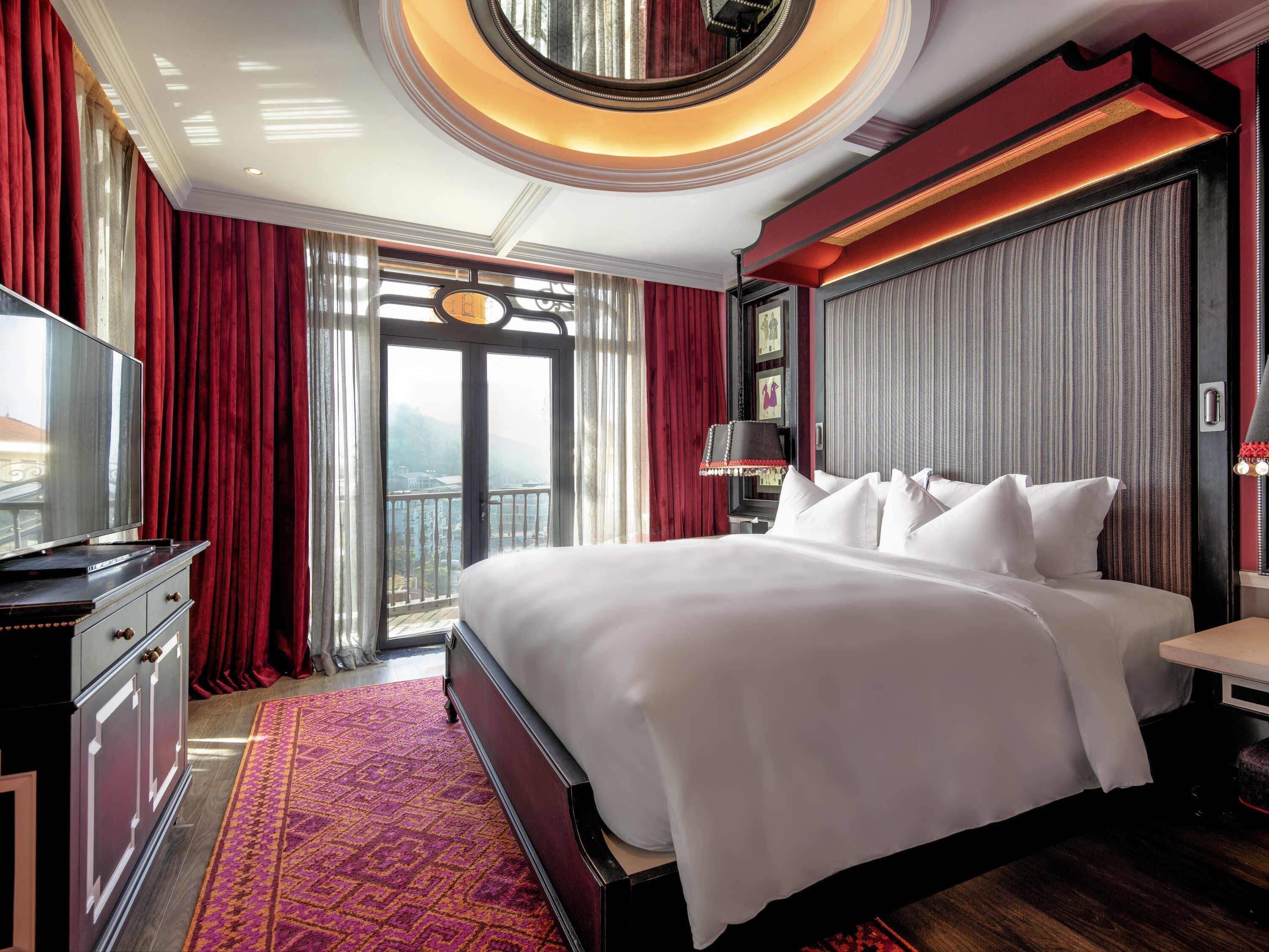 A hotel room with a large bed, a television, a desk, and a view of the outdoors.