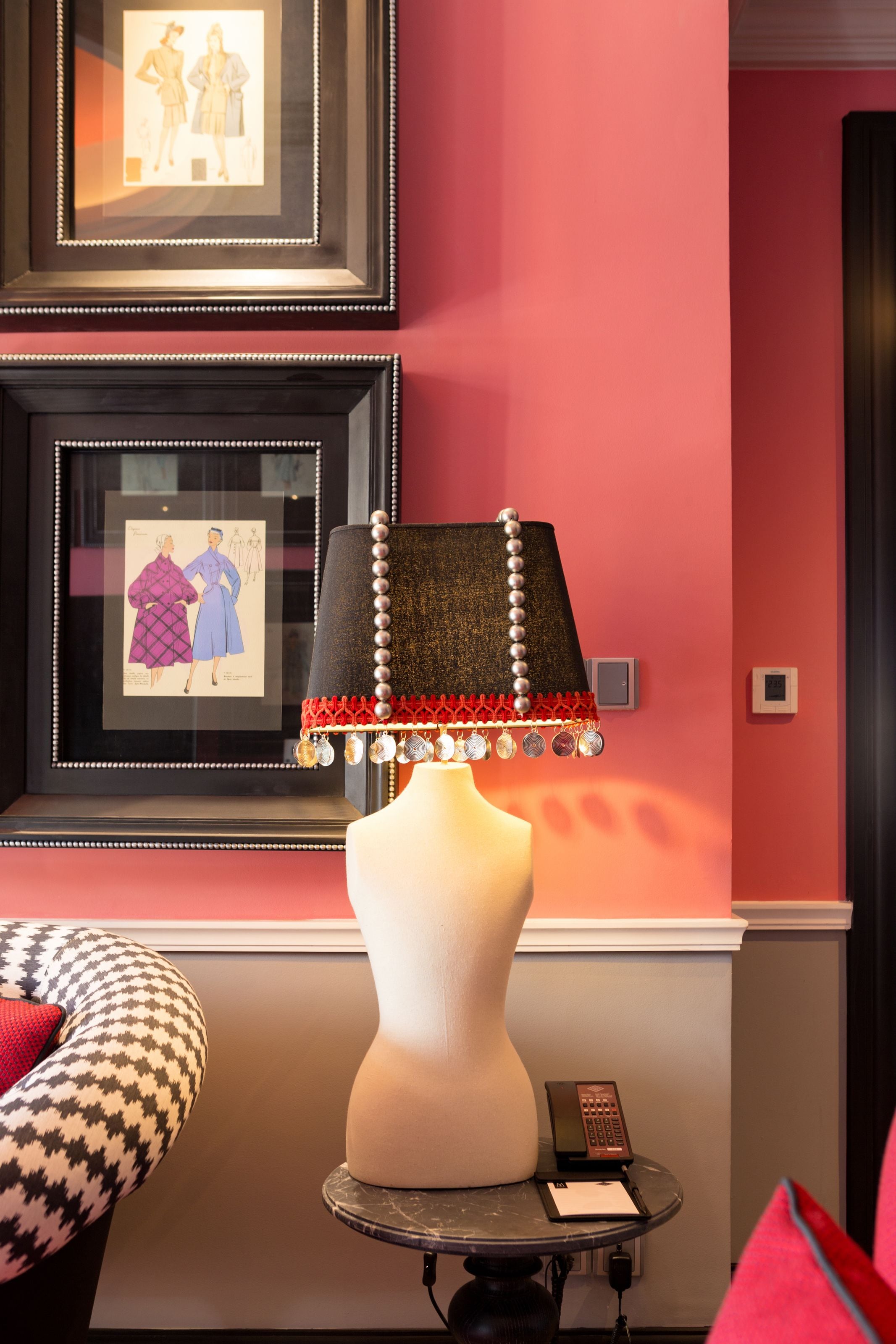 Une pièce avec une lampe blanche posée sur un piédestal, un tableau encadré accroché au mur et une chaise à motifs.