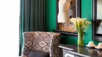 Un sillón estampado con un cojín negro, un armario de madera oscura con tiradores decorativos y un jarrón con flores blancas sobre una mesa.