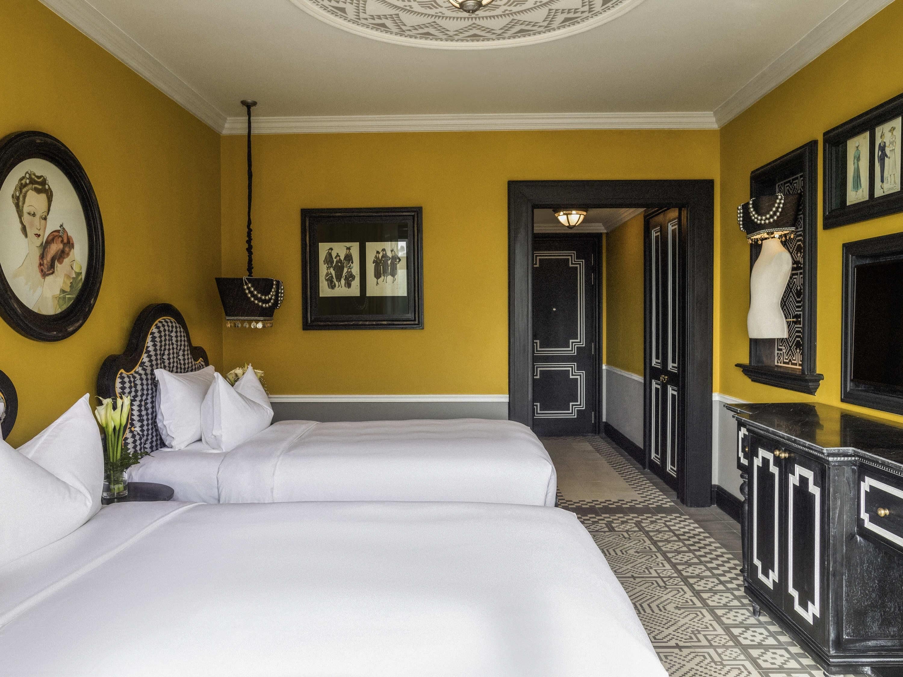 Een hotelkamer met twee bedden, een spiegel, een ingelijst schilderij, een kroonluchter en een vloer met patroon.