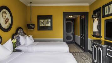 A hotel room with two beds, a mirror, a framed picture, a chandelier, and a patterned floor.