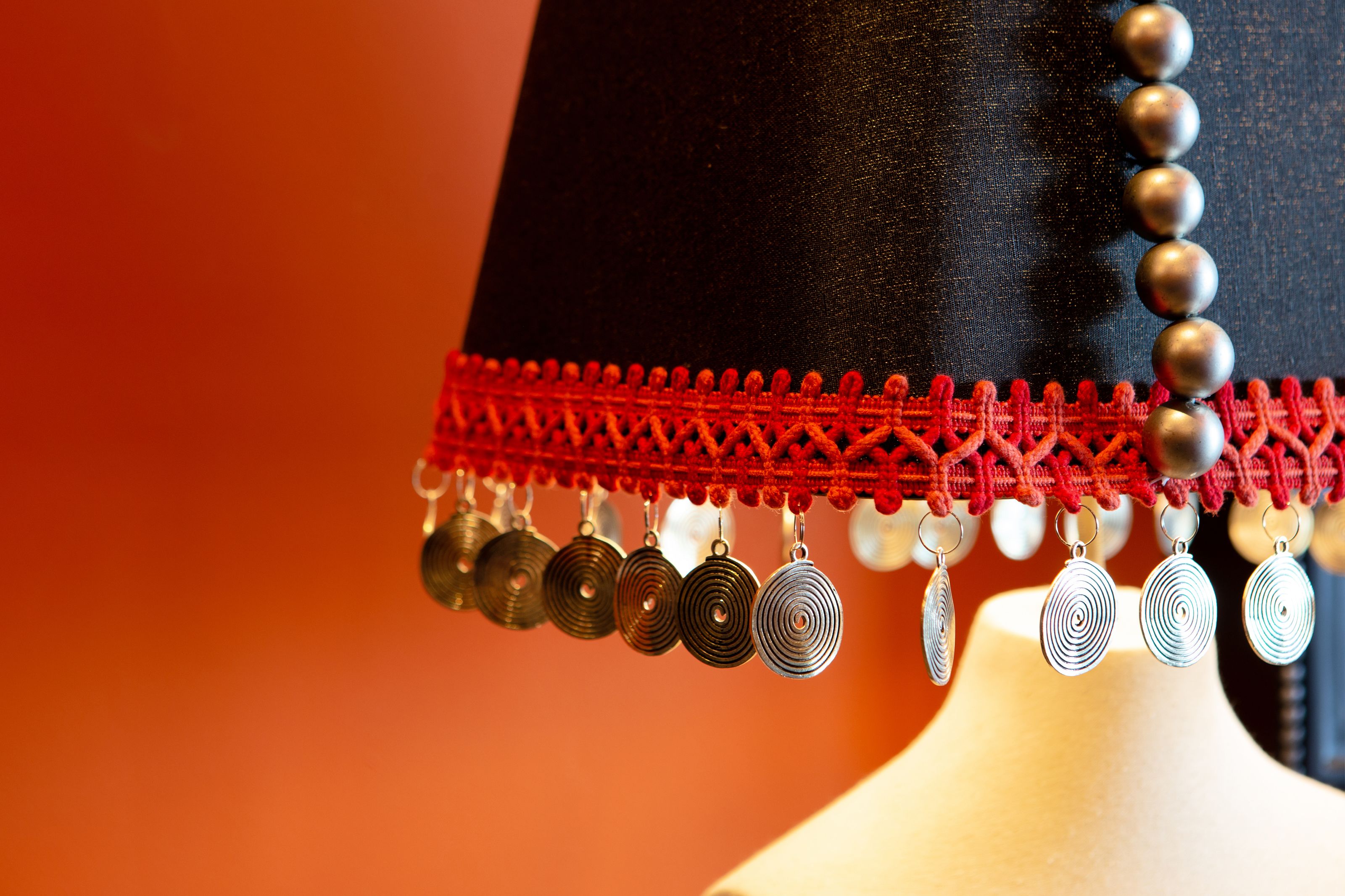 A close-up of a black garment with a red fringe and metallic circular ornaments.