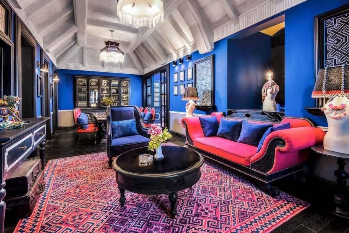 Una habitación con techo alto, paredes azules, un sofá rojo, una mesa de centro negra y un tapiz con diseño.