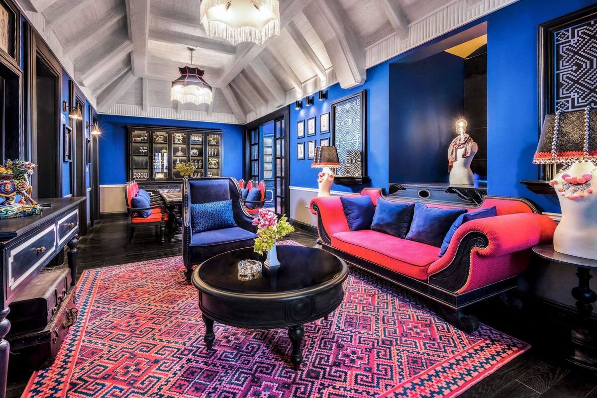 A room with a high ceiling, a patterned rug, a red and blue sofa, a black coffee table, and a chandelier.
