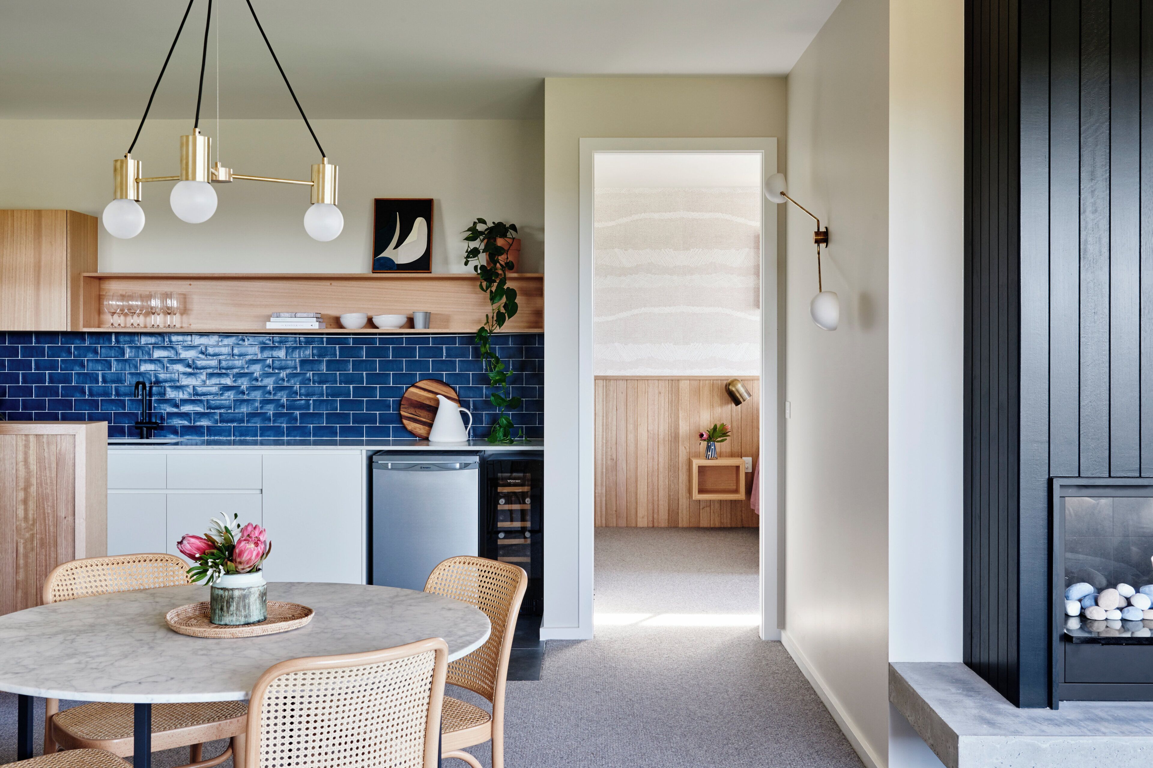 Eine moderne Küche mit blauer Rückwand, Holzschränken und einem Essbereich mit Korbstühlen.