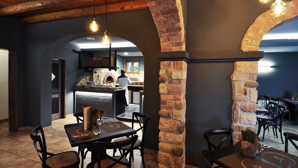 Restaurante com arcos de tijolo, área de cozinha e mesas preparadas para refeições.
