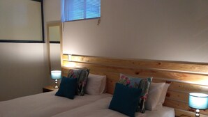 Una cama doble con cabecera de madera, dos mesitas de noche con lámparas y almohadas estampadas con motivos florales.