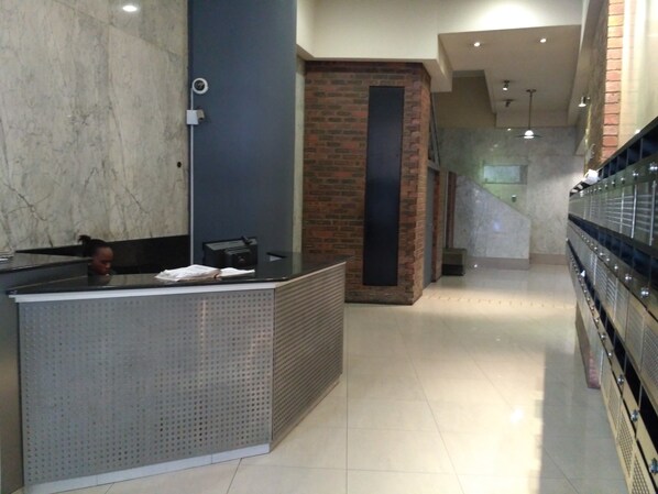 A reception area with a marble wall, a reception desk, a brick accent wall, and a staircase with a glass railing.
