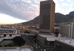 A modern building with a tall, vertical design, surrounded by a cityscape with mountains in the background. - At St. George's Mall (Cape Town)