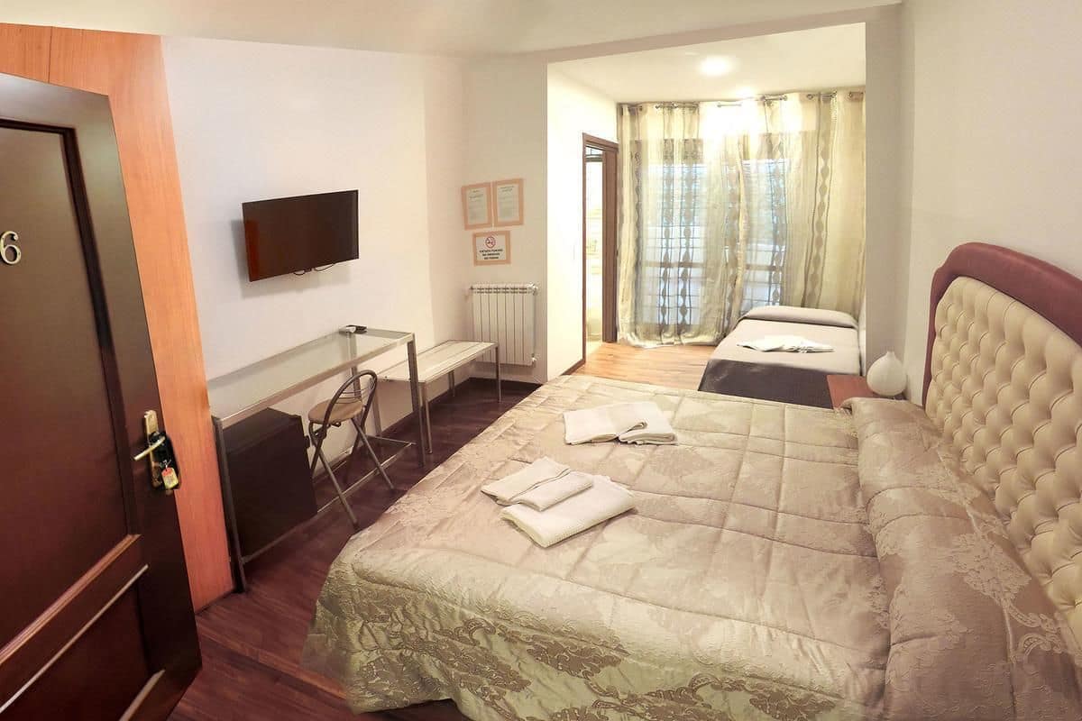 A hotel room with a large bed, a desk, a chair, a television, and a view of the outdoors through a window.