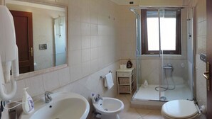 Casa de banho com duas pias, um bidé, uma sanita e um chuveiro com divisória de vidro, além de um espelho grande.