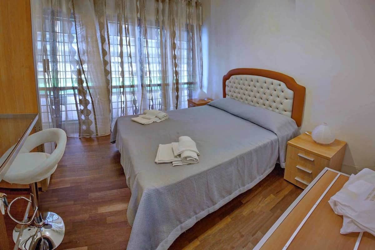 A hotel room with a bed, a chair, a bedside table, and a window with curtains.