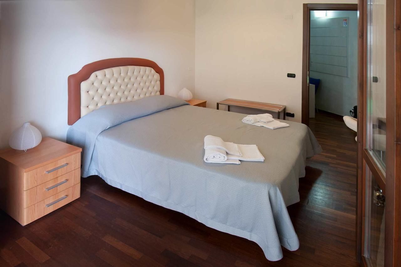 A neatly made bed with a headboard, a wooden nightstand with drawers, and a small bedside table.