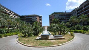 Pátio com uma fonte central, rodeado por palmeiras e um caminho pavimentado.