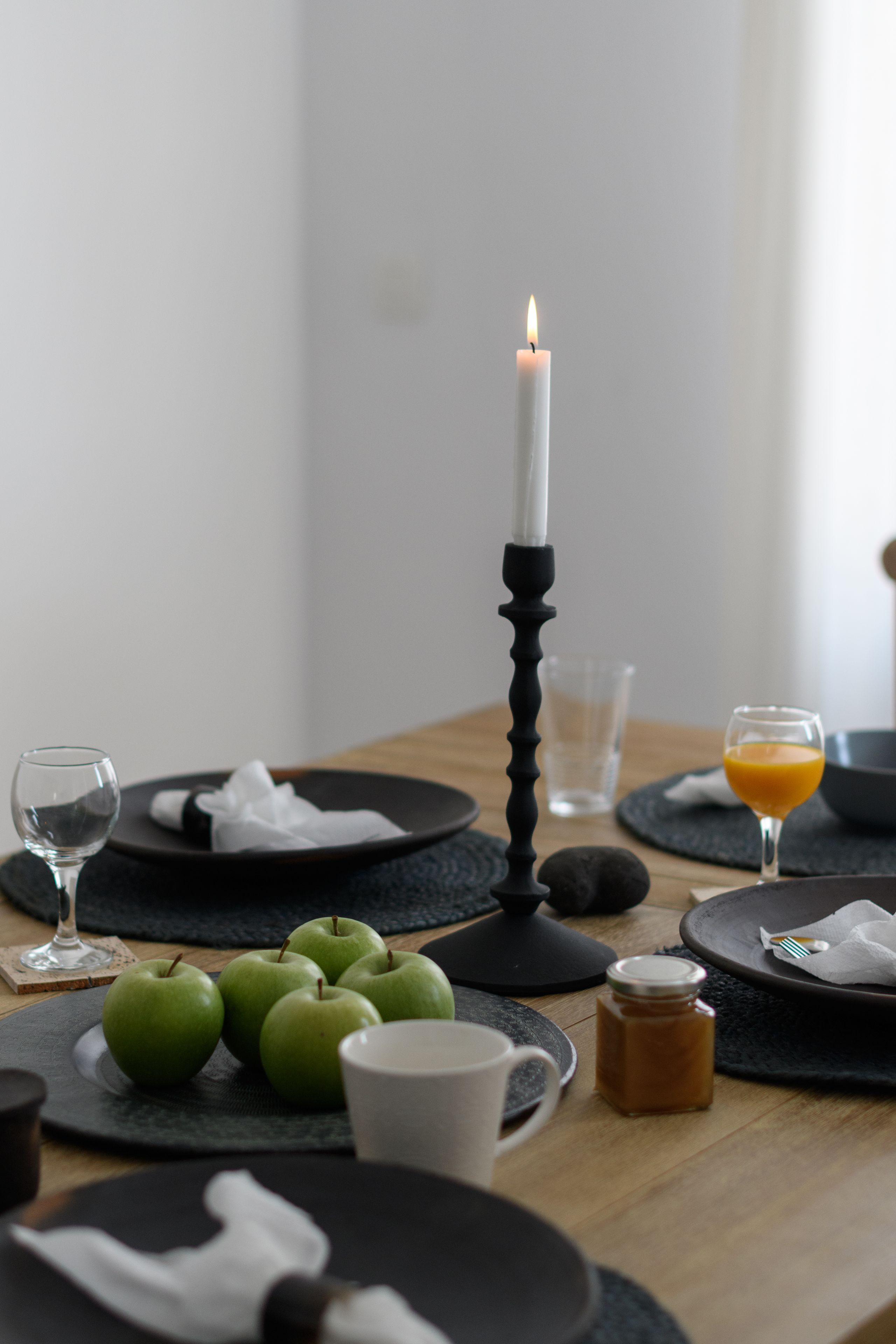Ein gedeckter Tisch mit Tellern, einer Kerze, Äpfeln, einem Glas Saft und einer Honigflasche.
