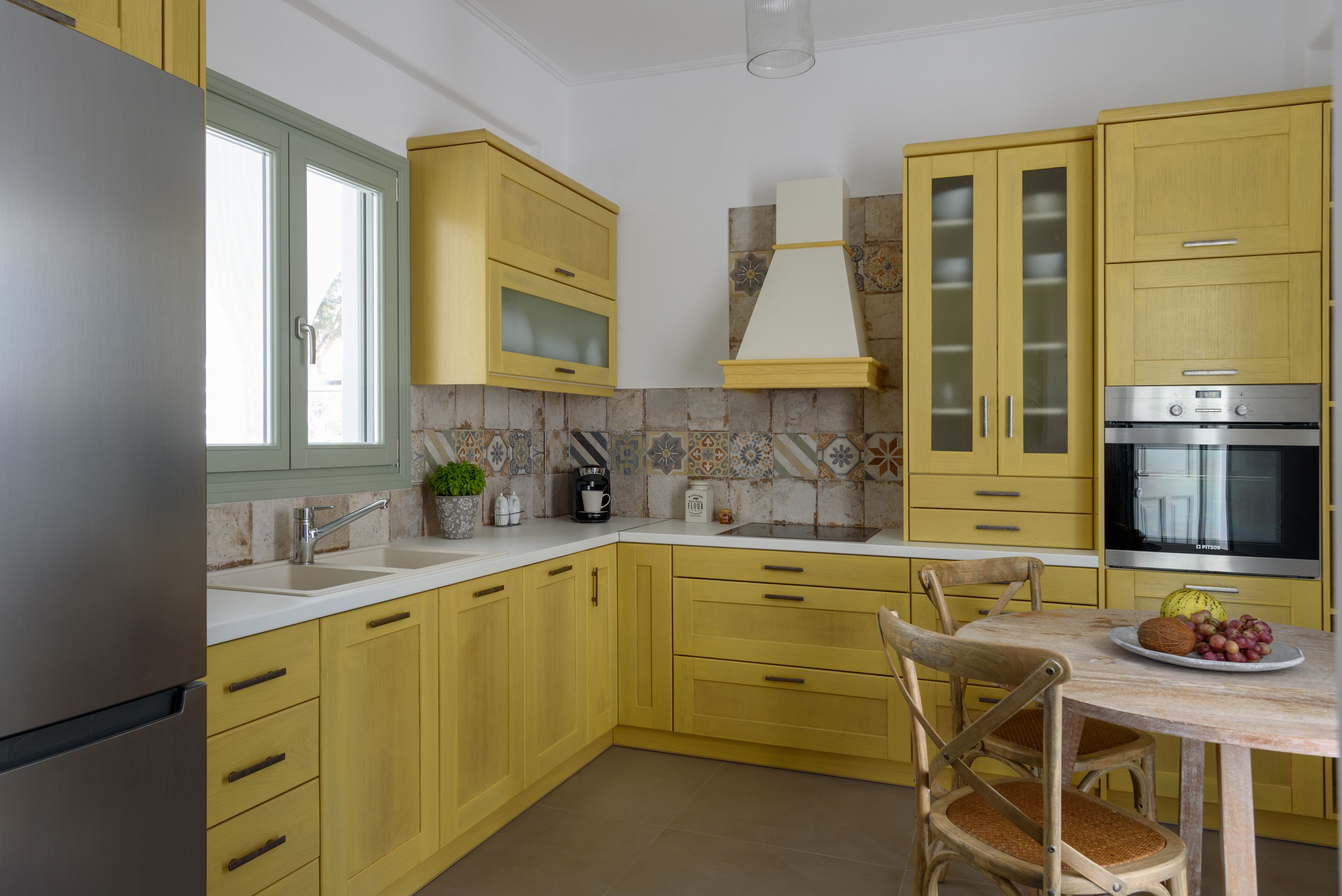A kitchen with yellow cabinets, a stainless steel refrigerator, a coffee maker, and a dining table with chairs.