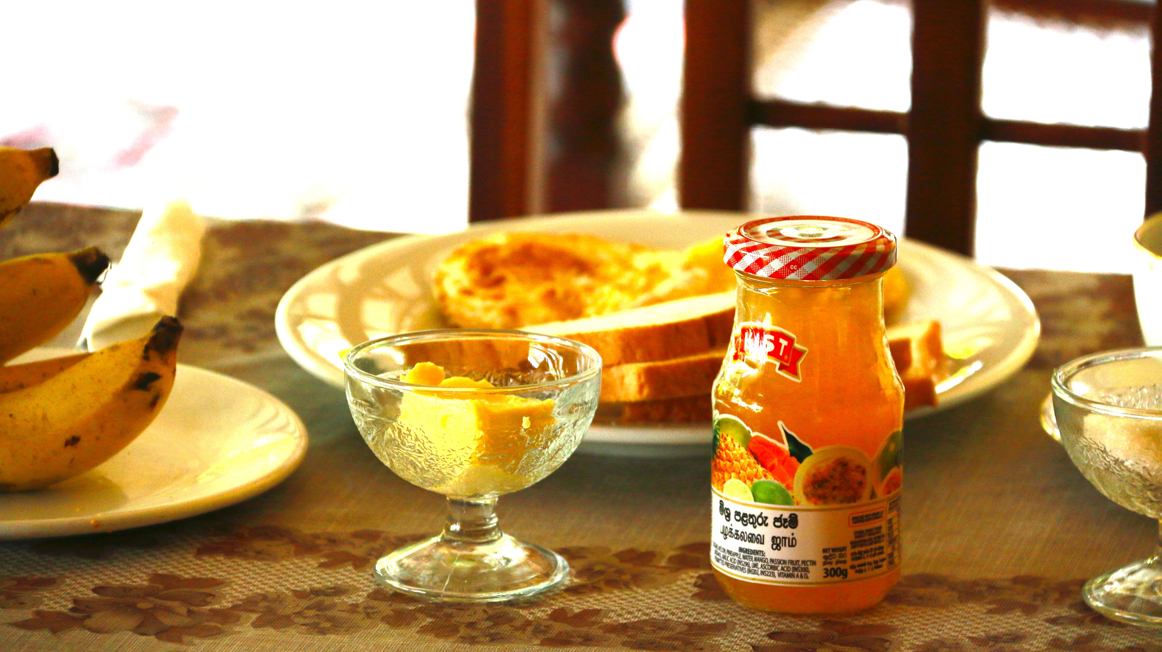 Une table avec une assiette de toasts, un bol en verre contenant une substance jaune et une bouteille de jus d’orange.