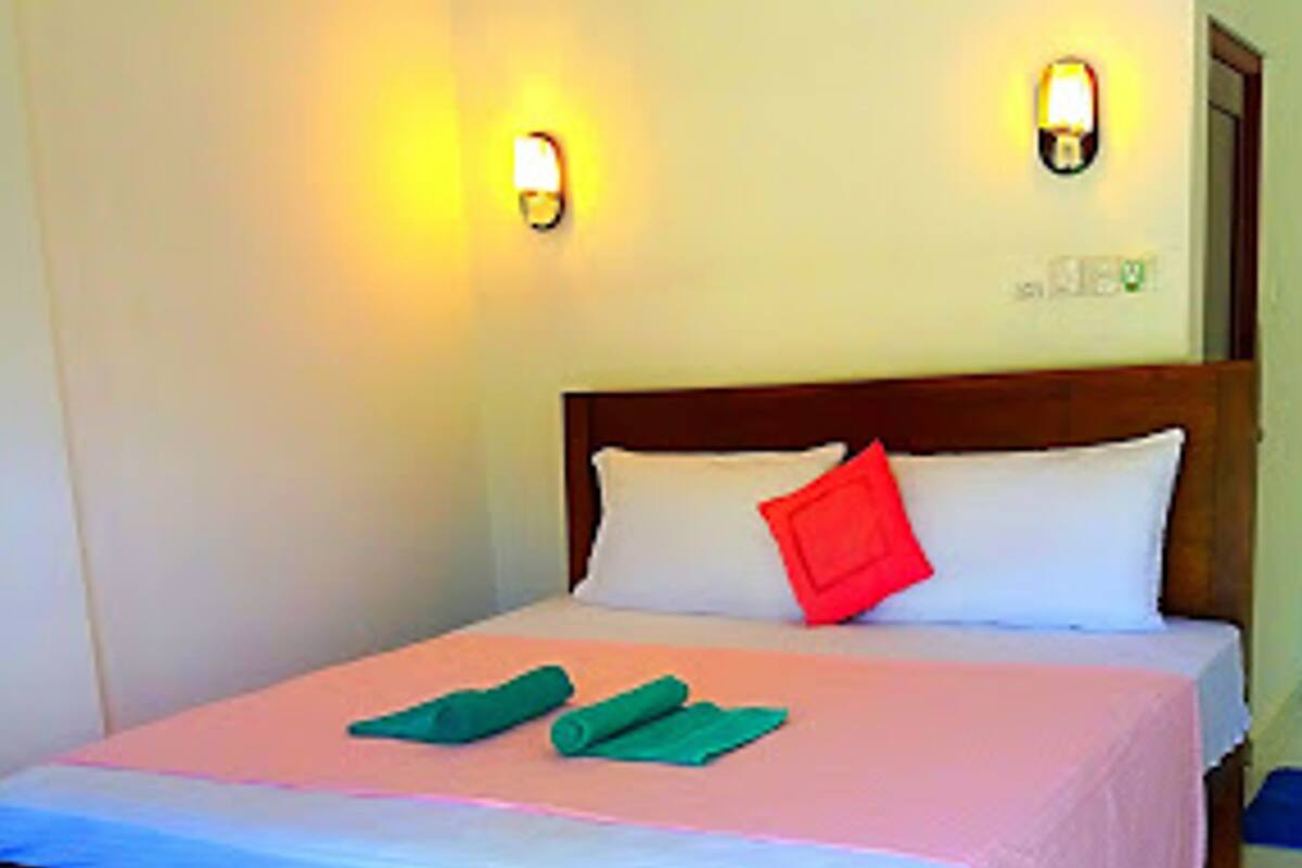 A neatly made bed with a wooden frame, a pink bedspread, and two green towels.