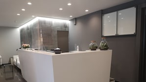 Un área de recepción moderna con un mostrador blanco, un espejo grande y dos jarrones de vidrio decorativos.
