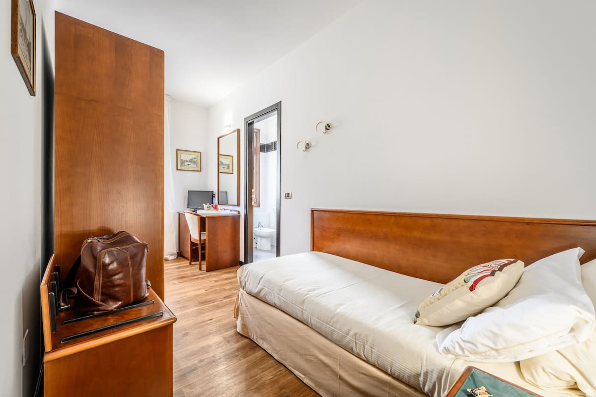 Ein Hotelzimmer mit einem hölzernen Bett, einem Schreibtisch mit Stuhl und einem Kleiderschrank.