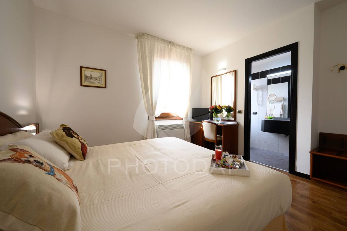 Ein Hotelzimmer mit Bett, Schreibtisch, Stuhl, einem Badezimmer-Spiegel und einem fensterbündigen Vorhang.