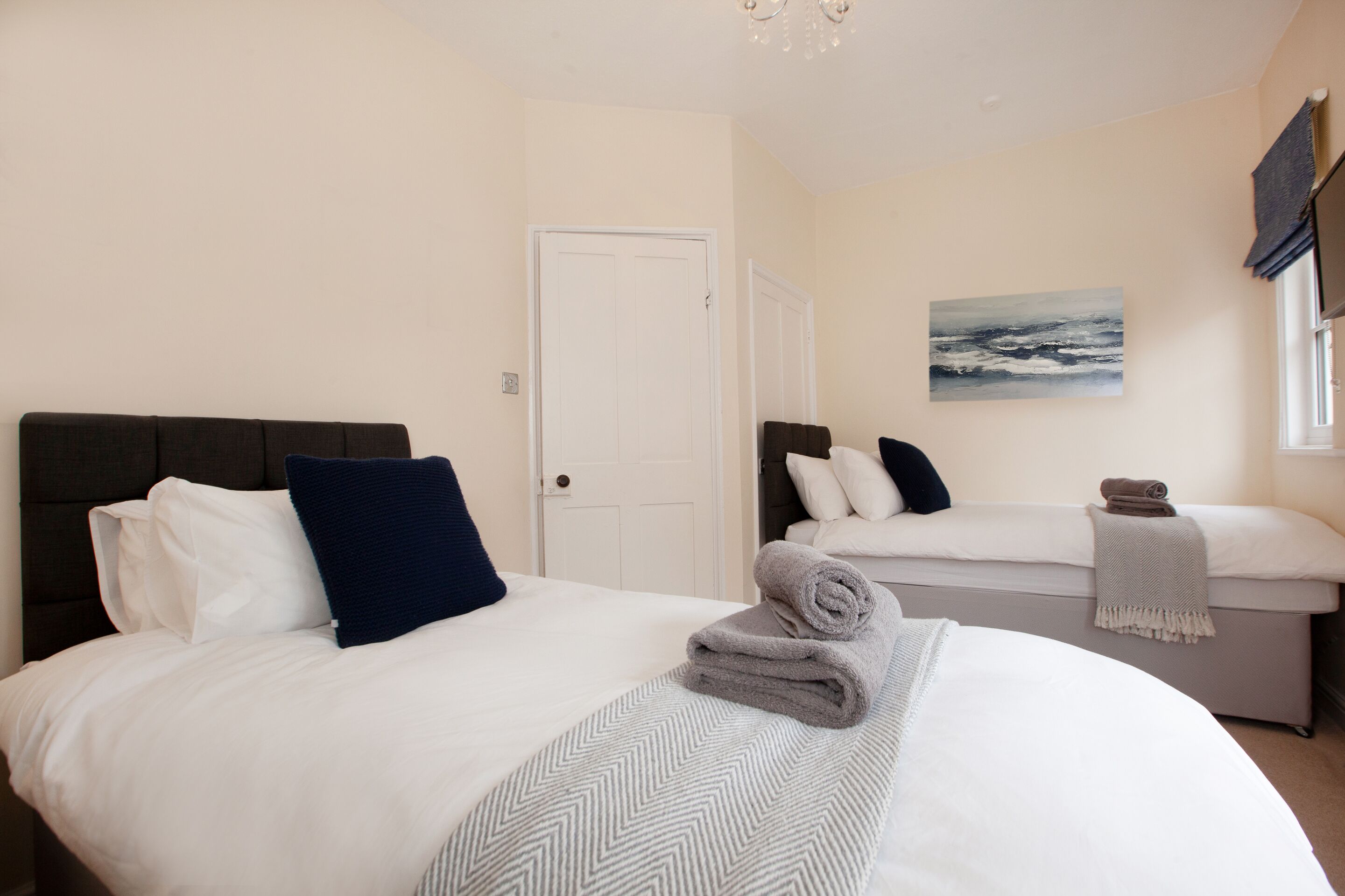 A hotel room with two beds, a painting on the wall, and a window with curtains.