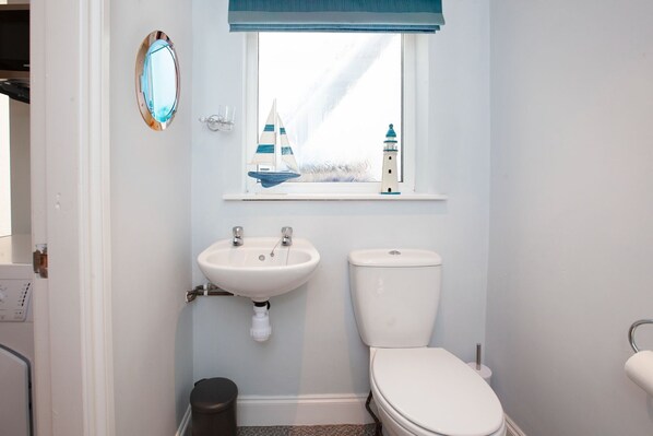 A small bathroom with a white sink, a white toilet, and a window with a view of a lighthouse and sailboat. - Clarence Cottage (Whitby)