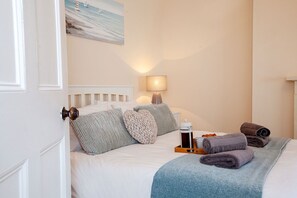 A neatly made bed with pillows, a bedside lamp, a tray with a mug and croissants, and a painting above the bed. - Clarence Cottage (Whitby)