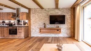 A modern kitchen with wooden cabinetry, a stone backsplash, and a flat-screen TV mounted above a wooden shelf. - Fetz Luxury Appartements (Steeg)