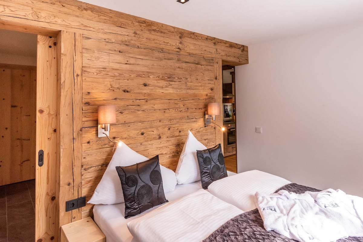 A bedroom with a wooden headboard, two bedside tables, a bed with white bedding, and two wall-mounted lamps.