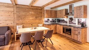 A modern kitchen with wooden cabinetry, a dining area with a table and chairs, and a built-in oven. - Fetz Luxury Appartements (Steeg)