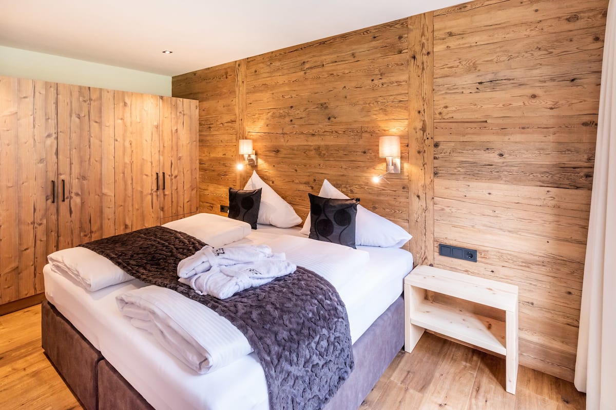 A modern bedroom with a wooden wall, a large bed with white linens, two bedside lamps, and a wooden bench.