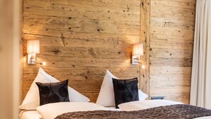A hotel room with a wooden headboard, two bedside lamps, a bed with white linens, and a dark throw blanket. - Fetz Luxury Appartements (Steeg)