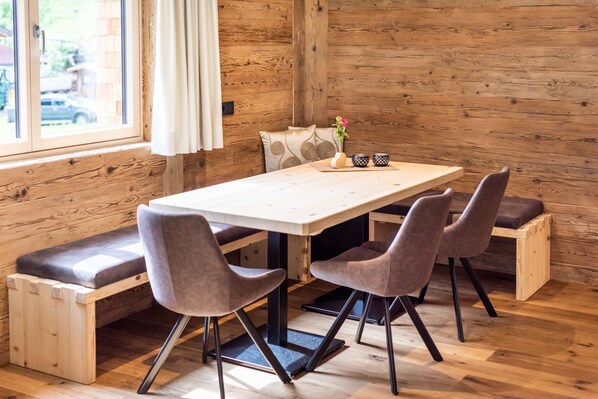A wooden interior with a table and four chairs, a bench, and a window with curtains. - Fetz Luxury Appartements (Steeg)