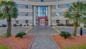 A multi-story hotel with a central entrance, surrounded by palm trees and a landscaped area.