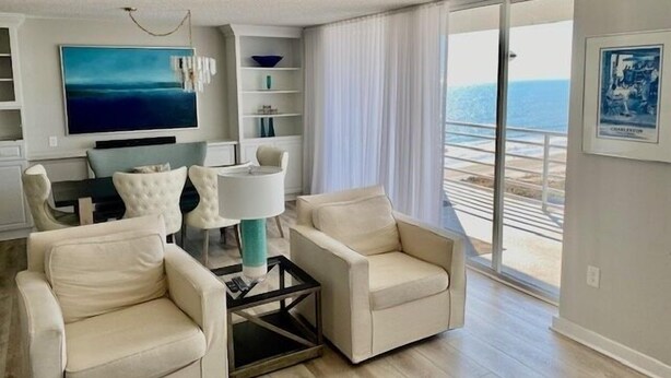 A modern living room with a large TV, comfortable seating, and a view of the ocean.