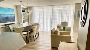 A modern living room with a dining area, a TV, and a large window with curtains.