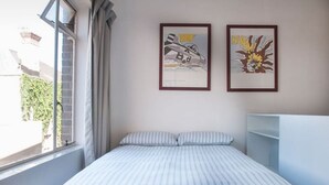 Un dormitorio con cama, dos cuadros enmarcados, una ventana con cortinas y un armario blanco.
