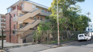 Un edificio de varios pisos con fachada color crema, una sección de ladrillo a la izquierda y una escalera metálica que da a los pisos superiores.
