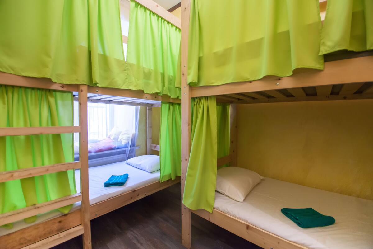 Une chambre avec des lits superposés, des rideaux verts et un plancher en bois.